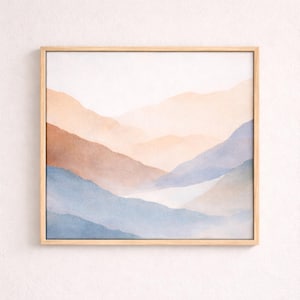 May include: Square framed art print featuring a watercolor landscape of layered mountains in shades of blue, peach, and brown. The artwork is set against a white background, and the frame is made of light-colored wood.