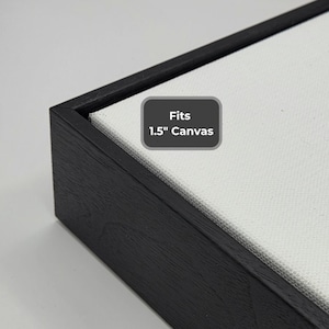 May include: Close-up of a black wooden frame with a white canvas. The frame has a dark finish and a beveled edge. A gray rectangle with the text "Fits 1.5" Canvas" is in the upper right corner.