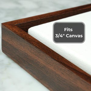 May include: Close-up of a dark brown wooden frame with a white canvas insert. The frame has a rectangular shape and a visible wood grain. A gray label reads "Fits 3/4" Canvas".
