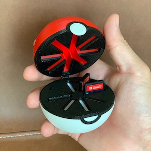 May include: A red and white Poke Ball shaped case with a black interior. The case is open and has slots for Nintendo Switch game cartridges. The text "Nintendo Switch" is visible on the game cartridges.