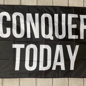 May include: Black flag with white text that reads "CONQUER TODAY".