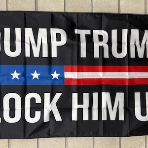 May include: Black flag with white text reading "DUMP TRUMP LOCK HIM UP." The flag features a blue stripe with white stars and red and white stripes, resembling a stylized American flag.
