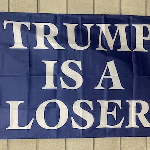 May include: A blue flag with white text that reads "TRUMP IS A LOSER".