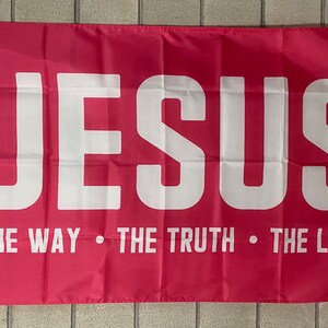 May include: A pink flag with the word "JESUS" in large white letters. Below the word "JESUS" is the text "THE WAY - THE TRUTH - THE LIFE" in white letters.