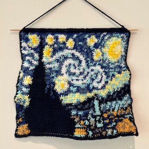 May include: A crocheted wall hanging depicting Vincent van Gogh's Starry Night. The artwork features a swirling sky in shades of blue, yellow, and white, with a dark cypress tree in the foreground.