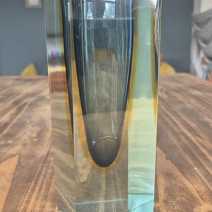 May include: A tall, rectangular glass vase featuring a thick, clear outer layer and a deep, dark blue inner core. The interior cavity is shaped like a rounded teardrop, surrounded by a warm, amber-toned glass transition that catches the light.