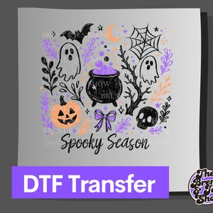May include: A DTF transfer featuring a Halloween-themed graphic with the text Spooky Season. The design includes a black cauldron with purple bubbles, ghosts, a pumpkin, a skull, a spider web, a bat, and a bow, accented with purple and orange foliage.