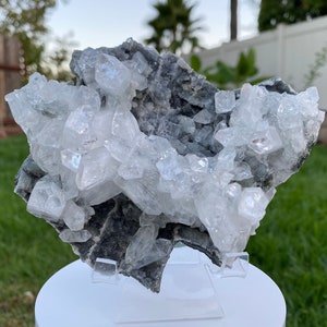 May include: A cluster of white celestite crystals on a gray matrix. The crystals are translucent and have a glassy luster. The matrix is rough and textured.
