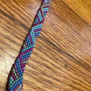 May include: A colorful friendship bracelet with a geometric pattern in shades of blue, green, purple, and red.