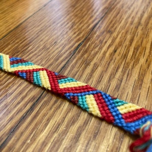 May include: A colorful friendship bracelet with a chevron pattern in red, yellow, blue, and green.