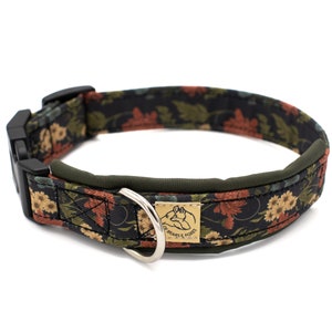 Könnte beinhalten: Ein schwarzes Hundehalsband mit einem Blumenmuster in Rot-, Gelb- und Grüntönen. Das Halsband hat ein grünes gepolstertes Futter und eine schwarze Schnalle. Das Halsband hat einen D-Ring aus Metall und ein goldenes Schild mit der Aufschrift "Heads & Tails".