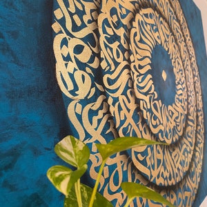 Puede incluir: Una pintura sobre lienzo azul con un dise&ntilde;o circular dorado de caligraf&iacute;a &aacute;rabe. El dise&ntilde;o est&aacute; en capas y crea un efecto de espiral.