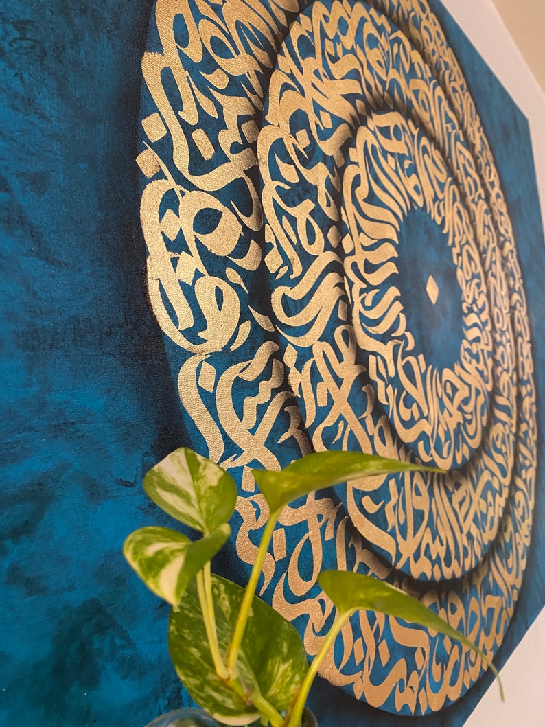 Puede incluir: Una pintura sobre lienzo azul con un dise&ntilde;o circular dorado de caligraf&iacute;a &aacute;rabe. El dise&ntilde;o est&aacute; en capas y crea un efecto de espiral.