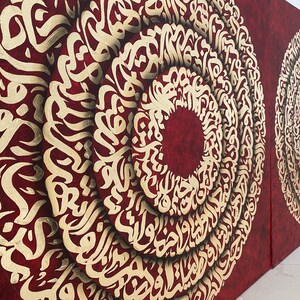 Puede incluir: Dos lienzos rojos con caligraf&iacute;a dorada en forma circular. La caligraf&iacute;a est&aacute; en escritura &aacute;rabe.