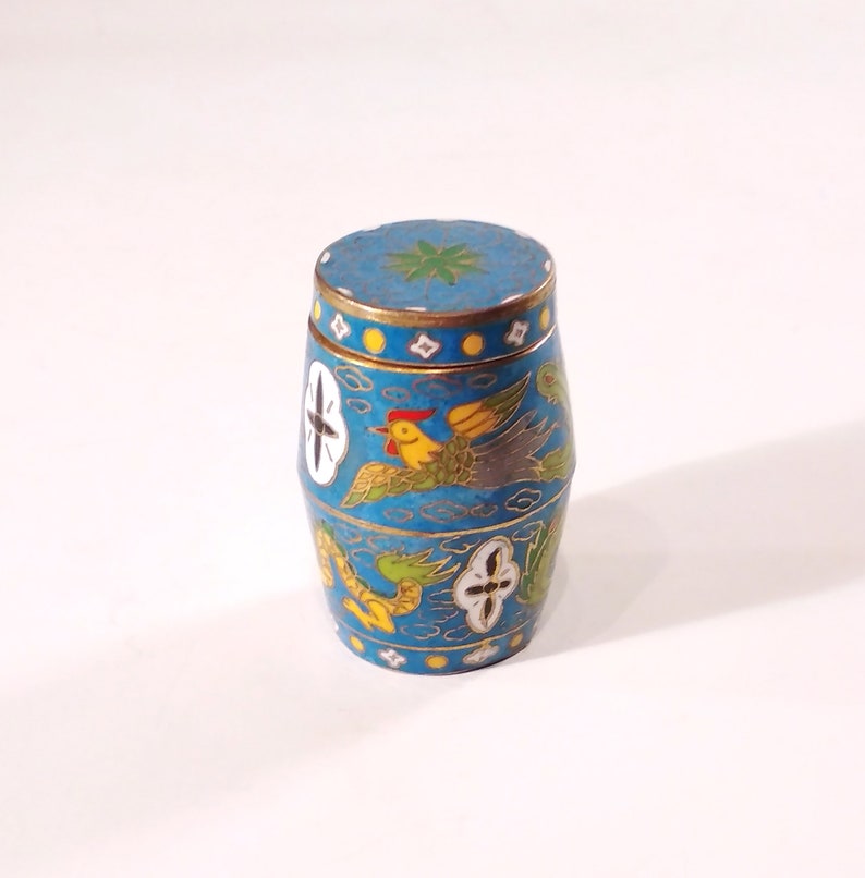 May include: A small, blue, cylindrical container with a lid, decorated with colourful birds and floral patterns. The container is made of metal and has a glossy finish.