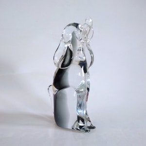 Pu&ograve; includere: Una statuetta di cane in vetro trasparente in posizione seduta, con le orecchie dritte e la coda alzata. La scultura presenta una sfumatura di nero e grigio all'interno del vetro, aggiungendo profondit&agrave;. Il cane &egrave; su sfondo bianco.