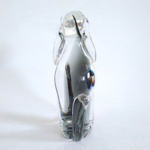 Pu&ograve; includere: Una scultura in vetro trasparente a forma di cane, con lunghe orecchie e coda. La figura &egrave; trasparente, lasciando passare la luce, su sfondo bianco. Un oggetto decorativo.