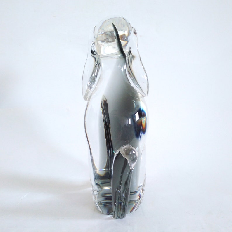 Pu&ograve; includere: Una scultura in vetro trasparente a forma di cane, con lunghe orecchie e coda. La figura &egrave; trasparente, lasciando passare la luce, su sfondo bianco. Un oggetto decorativo.