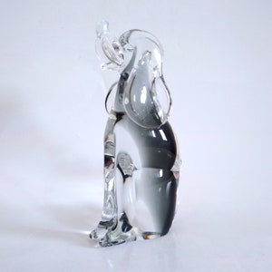 Pu&ograve; includere: Una scultura in vetro trasparente di un cane con un uccello appollaiato sulla testa. Il cane &egrave; seduto, con le orecchie abbassate. La scultura ha un effetto sfumato, che passa dal trasparente a un grigio fumoso.