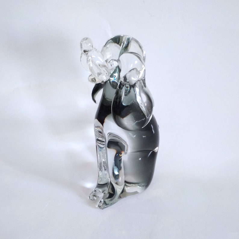 Pu&ograve; includere: Una scultura in vetro trasparente e grigio di un cane, in posizione seduta. La forma del cane &egrave; stilizzata, con tratti arrotondati e una superficie liscia. La scultura &egrave; posta su uno sfondo bianco.