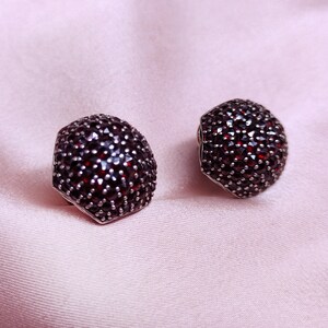 May include: A pair of silver earrings with a hexagonal shape, each earring is completely covered in small, dark red gemstones.
