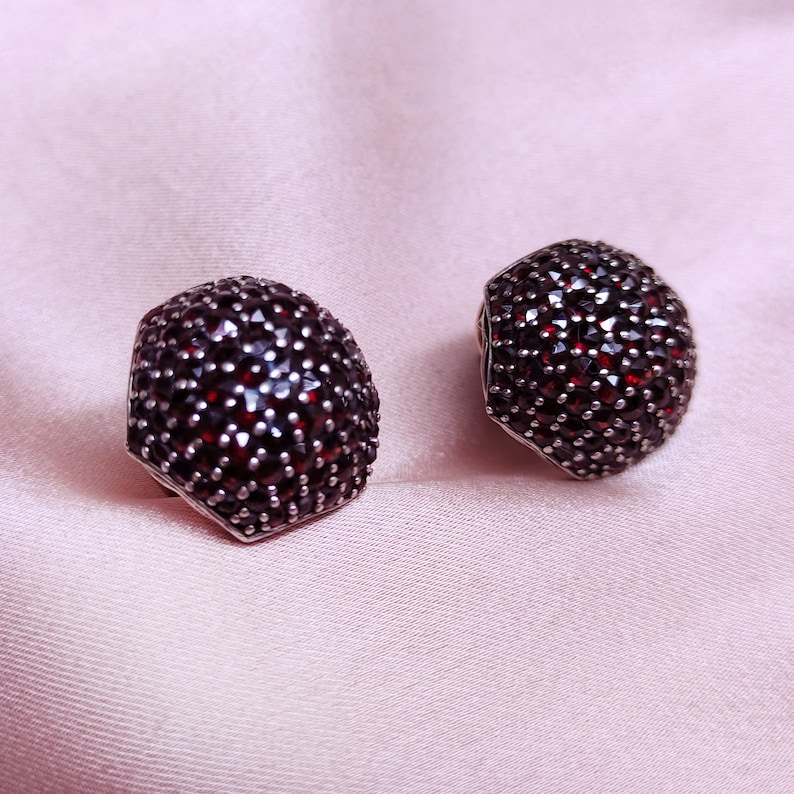 May include: A pair of silver earrings with a hexagonal shape, each earring is completely covered in small, dark red gemstones.