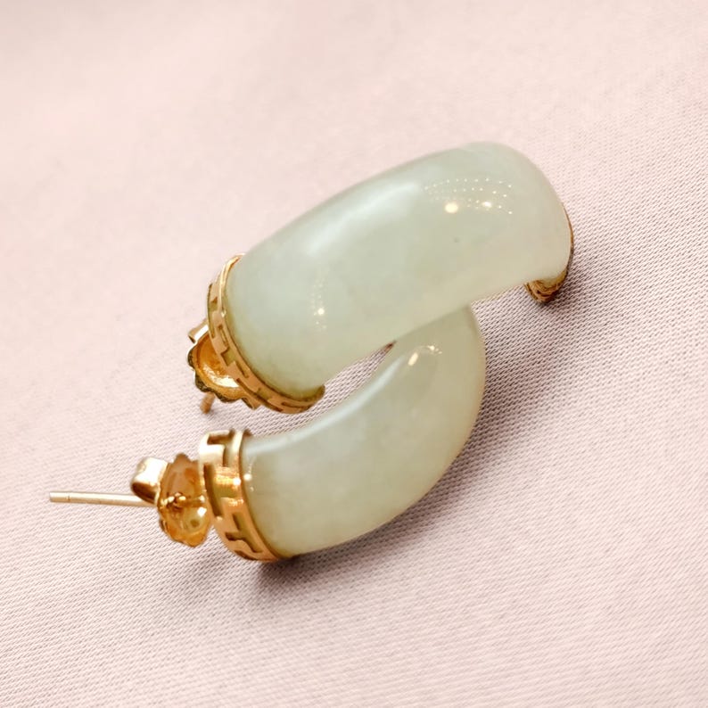 May include: A pair of jade hoop earrings with gold accents. The earrings have a curved, semi-circular design with a pale green hue. The gold settings add a touch of elegance to the jewelry.