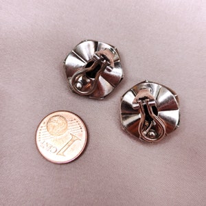 May include: A pair of silver tone clip-on earrings with a faceted design. The earrings are about the size of a UK penny.