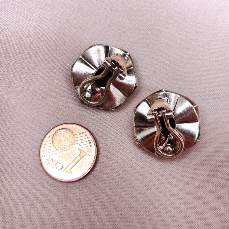 May include: A pair of silver tone clip-on earrings with a faceted design. The earrings are about the size of a UK penny.