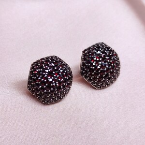 May include: A pair of silver earrings with a hexagonal shape, each earring is completely covered in small, dark red gemstones.