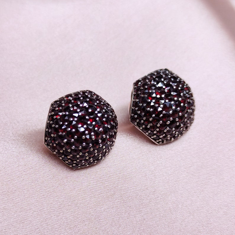 May include: A pair of silver earrings with a hexagonal shape, each earring is completely covered in small, dark red gemstones.