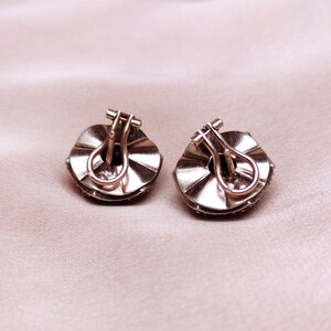 May include: A pair of silver tone earrings with a round, scalloped design. Each earring features a red gemstone in the centre.