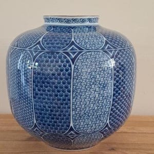 May include: A round ceramic vase featuring a blue and white colour palette. The surface is decorated with a series of vertical panels, each containing distinct geometric patterns including honeycombs, scales, and cross-hatching, with a rim border.
