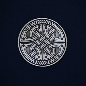 May include: A silver circular pendant with a detailed Celtic knot design. The knot is intricate and symmetrical, with a silver finish.