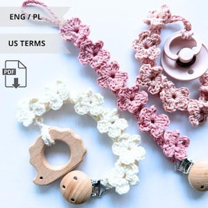Può includere: Tre clip per ciuccio per bambini con dettagli floreali all'uncinetto. Uno è bianco, un altro rosa e il terzo è un gradiente di rosa. Ogni clip ha un attacco in legno e una clip in metallo. Un ciuccio per bambini è attaccato a una delle clip.