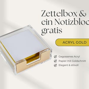 Puede incluir: Una caja de notas de acrílico transparente con una base y detalles dorados, que contiene una pila de papel de notas blanco con bordes dorados. El texto "ACRYL GOLD" se muestra en una etiqueta dorada.