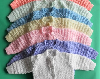 May include: A stack of seven knitted baby cardigans in various pastel colors, including pink, blue, yellow, and white. The cardigans are all made with a textured stitch and have a button closure.