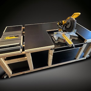 K&ouml;nnte beinhalten: Ein gro&szlig;er, ma&szlig;gefertigter Holzbearbeitungsplatz mit schwarzer Tischplatte und einer gelb-silbernen Gehrungss&auml;ge. Der Arbeitsplatz hat eine Tischkreiss&auml;ge und wird von einem hellen Holzrahmen getragen. Der Arbeitsplatz ist auf R&auml;dern.