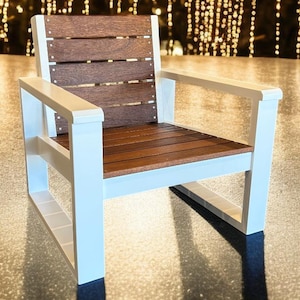 May include: A modern outdoor chair with a white frame and brown wooden seat and back. The chair has armrests and a slatted back design. The chair is made of durable materials and is suitable for patio or deck use.