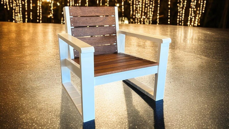 May include: A modern outdoor chair with a white frame and brown wooden seat and back. The chair has armrests and a slatted back design. The chair is made of durable materials and is suitable for patio or deck use.