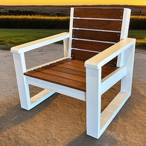 May include: A modern outdoor chair with a white frame and brown wooden seat and back. The chair has a slatted back and seat, and armrests. The chair is set against a backdrop of green grass and a sunset.