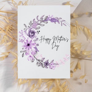Op de afbeelding: Een witte kaart met een paarse bloemenkrans en de tekst "Happy Mother's Day".