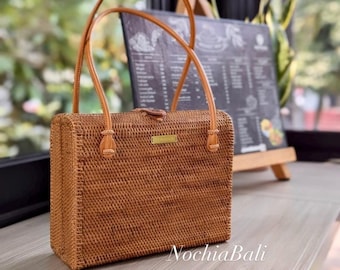 Könnte beinhalten: Eine braune geflochtene Handtasche mit einer Klappe und zwei Ledergriffen. Die Tasche liegt auf einer Holzoberfläche.