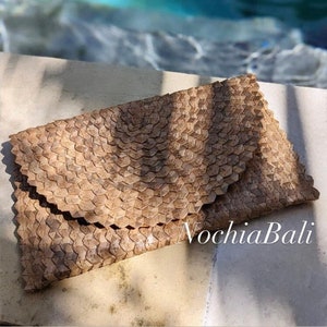 K&ouml;nnte beinhalten: Eine hellbraune geflochtene Clutch mit geometrischem Muster. Die Clutch ist aus nat&uuml;rlichen Materialien gefertigt und hat einen einzigartigen, handgefertigten Look. Der Text "NochlaBali" ist in der rechten unteren Ecke des Bildes sichtbar.