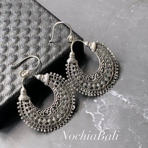 Könnte beinhalten: Ein Paar silberne Filigran-Creolen mit einem zarten, filigranen Design. Die Ohrringe sind groß und haben eine Halbmondform.