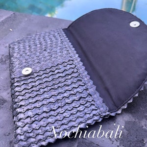 K&ouml;nnte beinhalten: Eine schwarze geflochtene Clutch mit Magnetverschluss. Die Clutch ist ge&ouml;ffnet und das Innere ist mit schwarzem Stoff ausgekleidet. Die Clutch hat ein geflochtenes Muster und ist aus einem strukturierten Material gefertigt.