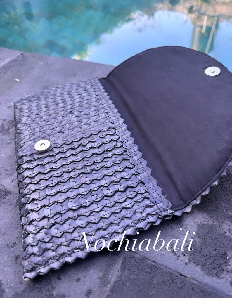 K&ouml;nnte beinhalten: Eine schwarze geflochtene Clutch mit Magnetverschluss. Die Clutch ist ge&ouml;ffnet und das Innere ist mit schwarzem Stoff ausgekleidet. Die Clutch hat ein geflochtenes Muster und ist aus einem strukturierten Material gefertigt.