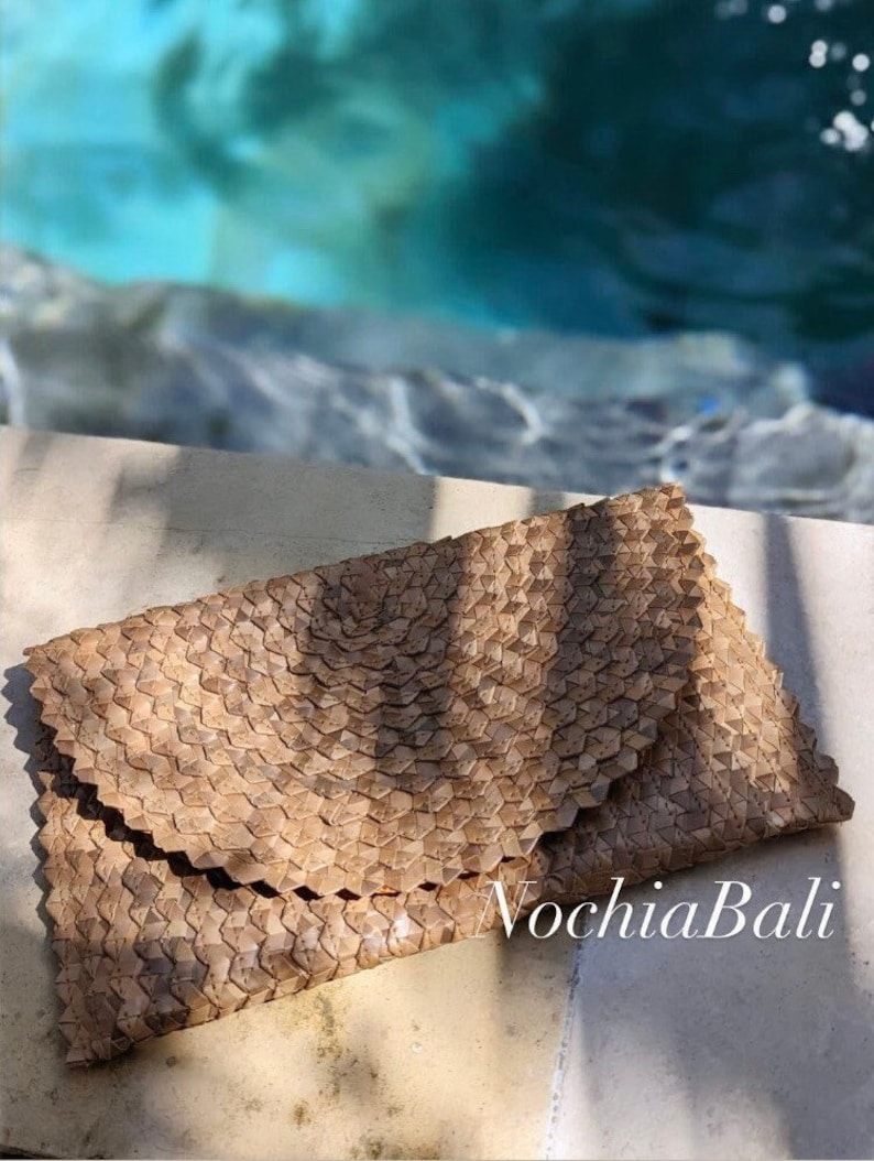 K&ouml;nnte beinhalten: Eine hellbraune geflochtene Clutch mit geometrischem Muster. Die Clutch ist aus nat&uuml;rlichen Materialien gefertigt und hat einen einzigartigen, handgefertigten Look. Der Text "NochlaBali" ist in der rechten unteren Ecke des Bildes sichtbar.