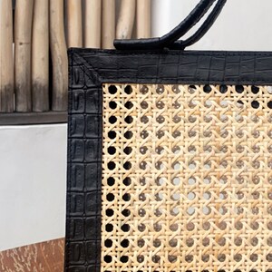 May include: A black leather tote bag with a woven rattan panel. The bag has a top handle and a black crocodile embossed leather trim.