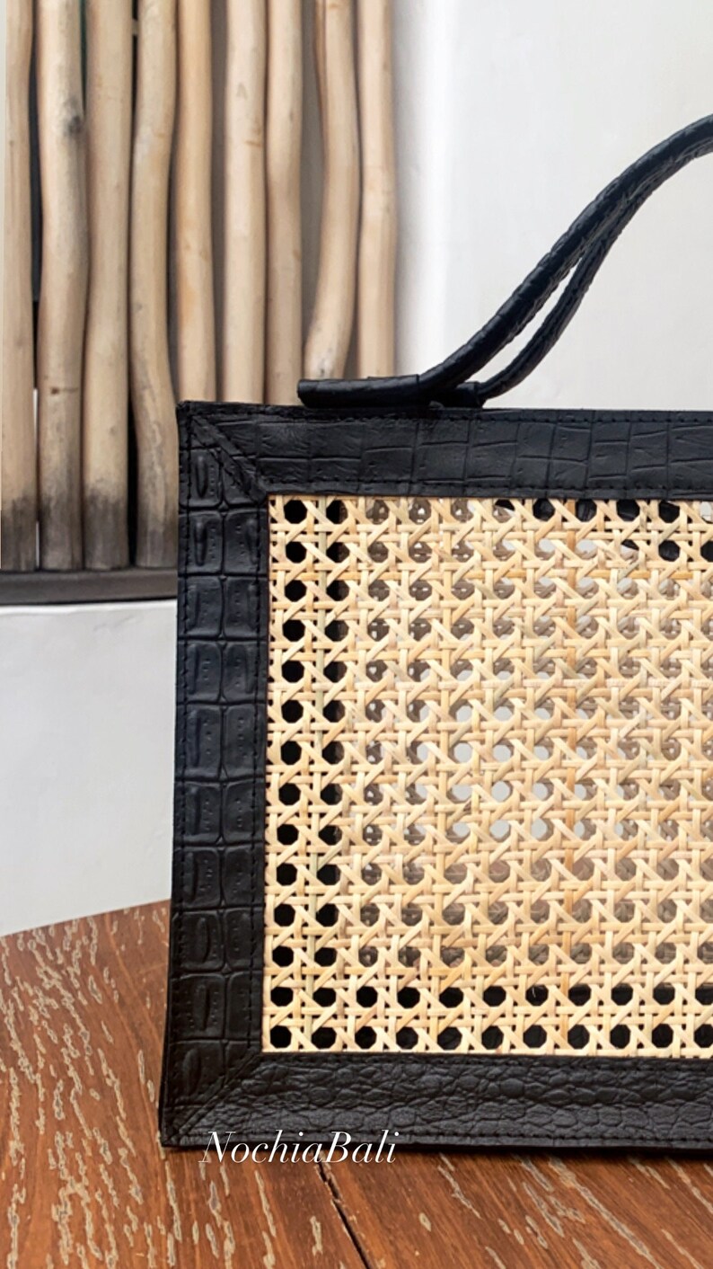 May include: A black leather tote bag with a woven rattan panel. The bag has a top handle and a black crocodile embossed leather trim.